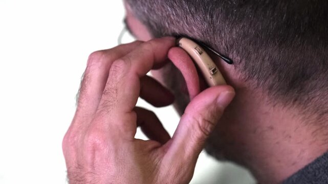 Close-up of a man with hearing impairment inserting a modern digital behind-the-ear hearing aid. Isolated on a white background