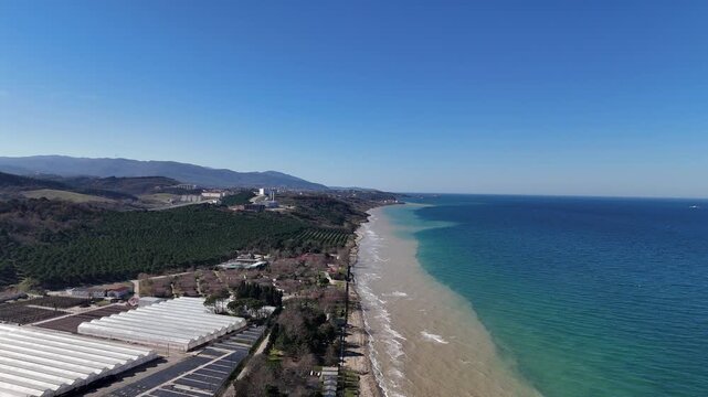 Aerial footage of a beautiful sea beach with clear water and gentle waves along the sandy shoreline. Natural coastal landscape ideal for travel, tourism, summer, vacation, relaxation, nature, and seas