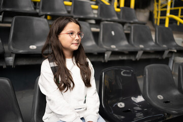 Teenage girl in glasses resting on stadium seat, education tourism sport and leisure concept