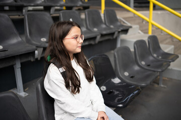 Happy teenage girl with backpack sitting at football stadium, exploration learning and vacation concept