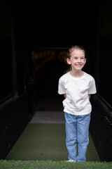 Vertical photo of funny cheerful girl in t shirt and jeans making faces on dark background, childhood fun emotion concept