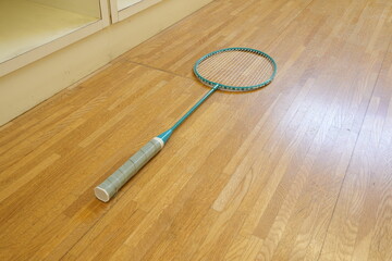 A tennis racket is laying on a wooden floor. The racket is blue and has a white handle. The floor is made of wood and he is a hardwood floor