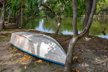 An old white wooden boat standing upside down on the shore of a lake on a sunny summer day