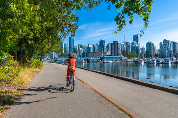 Fototapeta premium Tourist riding bicycle in stanley park with vancouver skyline in background