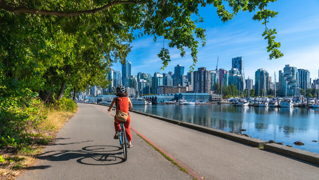 Woman cycling in stanley park with vancouver skyline in background - Powered by Adobe