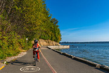 Obraz premium Woman cycling along stanley park seawall in vancouver, british columbia