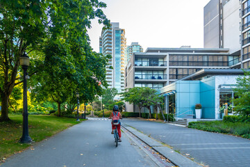Naklejka premium Woman riding bicycle in city park near modern buildings in vancouver