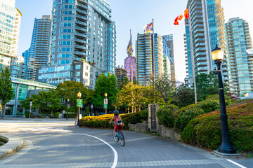 Obraz premium Student cycling in downtown vancouver with canadian flags waving