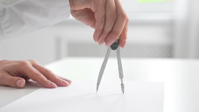 Hand Using Compass to Draw on White Paper