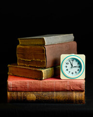 Vintage books stacked neatly, accompanied by a classic alarm clock against a dark background, evoking themes of education, time, and knowledge. The rustic textures add an antique charm.