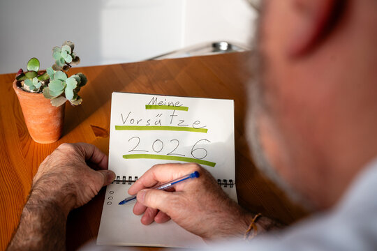 Mann schreibt Vorsätze für 2026 in Notizbuch am Holztisch - Powered by Adobe