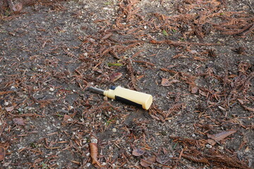 A yellow object is laying on the ground. It is a lighter. The ground is covered in leaves and dirt