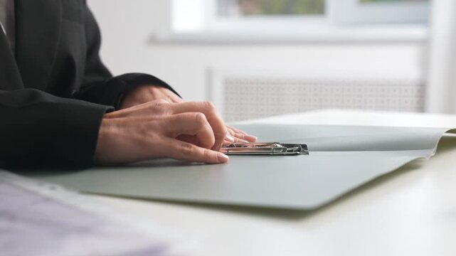 Hands open a folder and insert documents into plastic files.