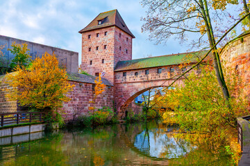 Fronveste building and part of old city wall and bridge system in Nuremberg, Germany, reflected in Pegnitz River. Autumnal scene with historic red sandstone architecture and lush surrounding foliage