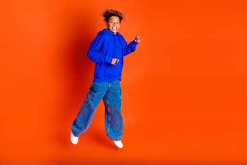 Joyful young boy jumps in blue hoodie on bright orange background for lifestyle advertising and...