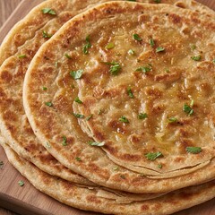 Golden brown layered flatbread paratha stacked on a wooden board garnished with fresh green cilantro herbs and glistening with oil a close up studio shot