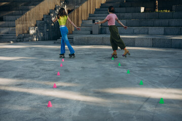 Pair friends on quads skates weave around colored cones on cement plaza