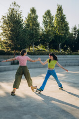 Women skaters join hands to show spinning move on quad skates in half-split position at sunset