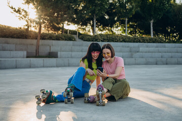 Young woman shows pictures on smartphone to girl friend on skating ground
