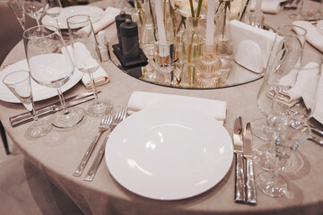 A round table is set with white plates, wine glasses, and silverware ready for guests. Centerpieces include small vases, and the table is covered with a light tablecloth