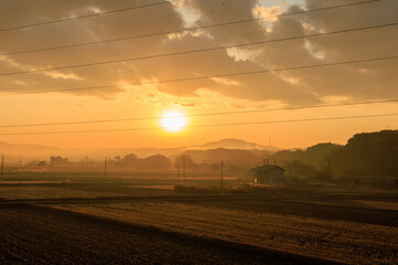 冬の田園地帯に昇る朝日とオレンジ色の空・日本の12月の早朝風景

