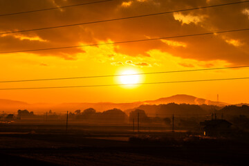 冬の田園地帯に昇る朝日とオレンジ色の空・日本の12月の早朝風景



