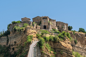 Fototapeta premium Italy - Bagnoregio - Civita di Bagnoregio - Close view of entrance gate and houses atop stratified tuff cliff above pedestrian bridge and valley