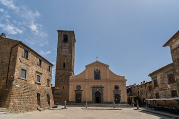 Italy - Bagnoregio - Civita di Bagnoregio - Piazza San Donato with church and bell tower framed by stone houses under clear sky, wide perspective