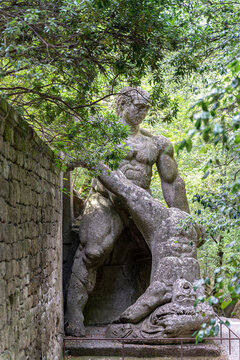 Italy - Bomarzo - Sacro Bosco - Hercules and Cacus monumental sculpture carved in peperino stone beneath trees along a mossy garden wall