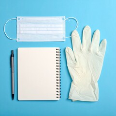 Flat lay of a light blue background with a face mask, notepad, pen, and latex gloves