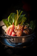 Spicy mala hot pot with sliced raw meat, shiitake mushrooms, and fresh vegetables in a stainless steel pot. Traditional Chinese Szechuan cuisine concept, dark moody lighting, vertical composition.