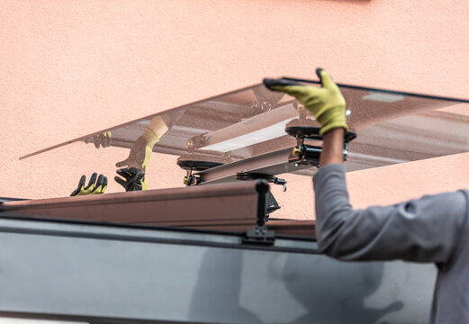 Workers install patio roofing with steel and glass