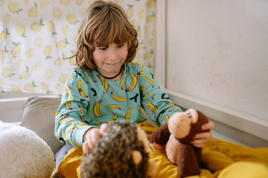 Child plays with stuffed animals in bedroom during daylight hours