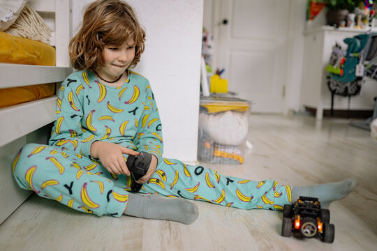 Boy plays with toy car in pajamas in cozy bedroom setting during afternoon