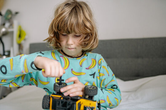 Boy plays with toy in bedroom while wearing pajamas and sitting on bed