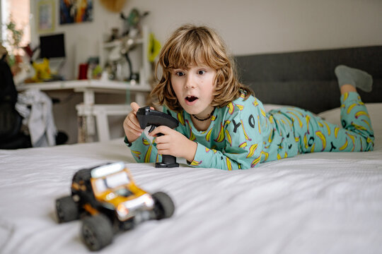 Boy in pajamas plays with remote-controlled toy in bedroom during morning