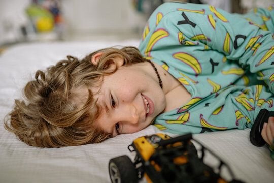 Boy plays with toy car in bedroom while wearing pajamas at home during daytime