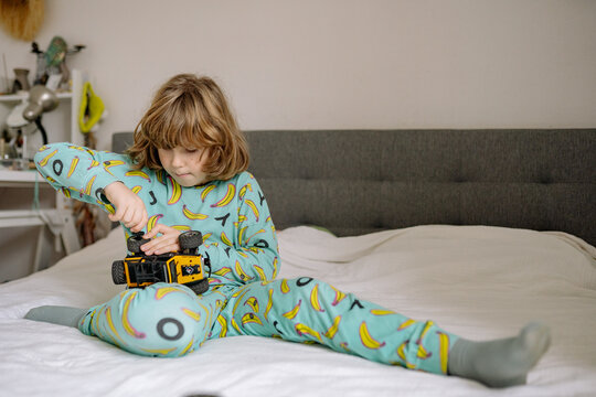 Child plays with a toy truck while sitting on bed in pajamas in a bedroom