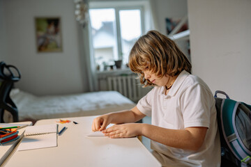 Fototapeta premium Boy engages in craft activity while sitting at a desk in his room during the day