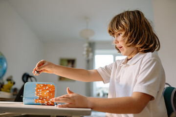 Boy making crafts at a table in his room with colorful materials on a sunny day