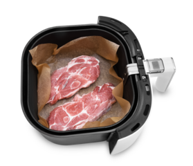 Raw pork neck steaks on parchment paper inside an air fryer basket, isolated on a white background.