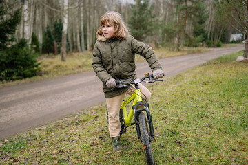 Fototapeta premium Child rides bike on a dirt path surrounded by trees during daytime in a quiet outdoor setting