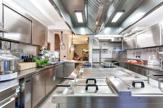 Modern restaurant kitchen with central stove, fresh herbs, utensils, and prep stations&mdash;ideal for gourmet cooking and foodservice operations.