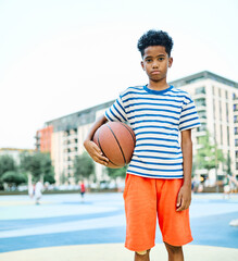 Fototapeta premium African american boy smiling, standing playing basketball on a colorful basketball court