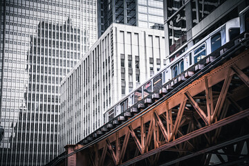 Naklejka premium Dramatic view of the iconic Chicago L elevated train and rusted tracks against a backdrop of modern, vertical skyscraper windows. Urban contrast and infrastructure.