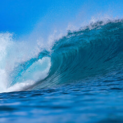 Massive blue ocean wave curling, bright turquoise barrel breaking with foamy crest and spray, sunlight