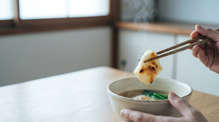 箸で焼き餅を掴む手とお雑煮のお椀、お正月の伝統的な和食シーン