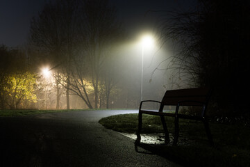 A bench in a park on a quiet foggy winters night in a park