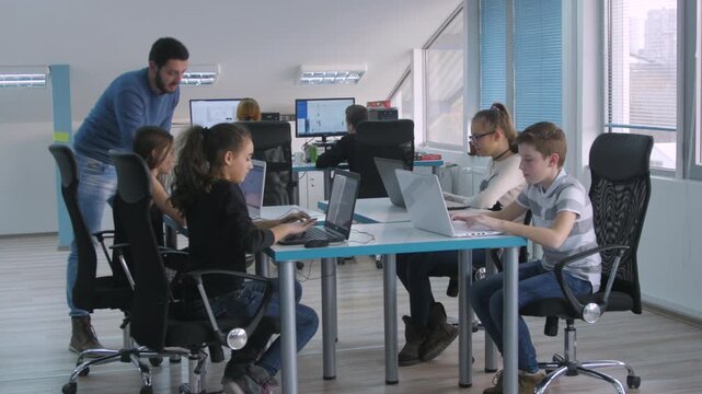 Teacher mentoring students working on laptops in modern bright classroom during STEM lesson