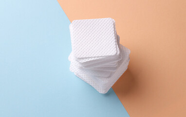Stack of Square cotton cosmetic pads for makeup removal on blue pink background. Beauty concept